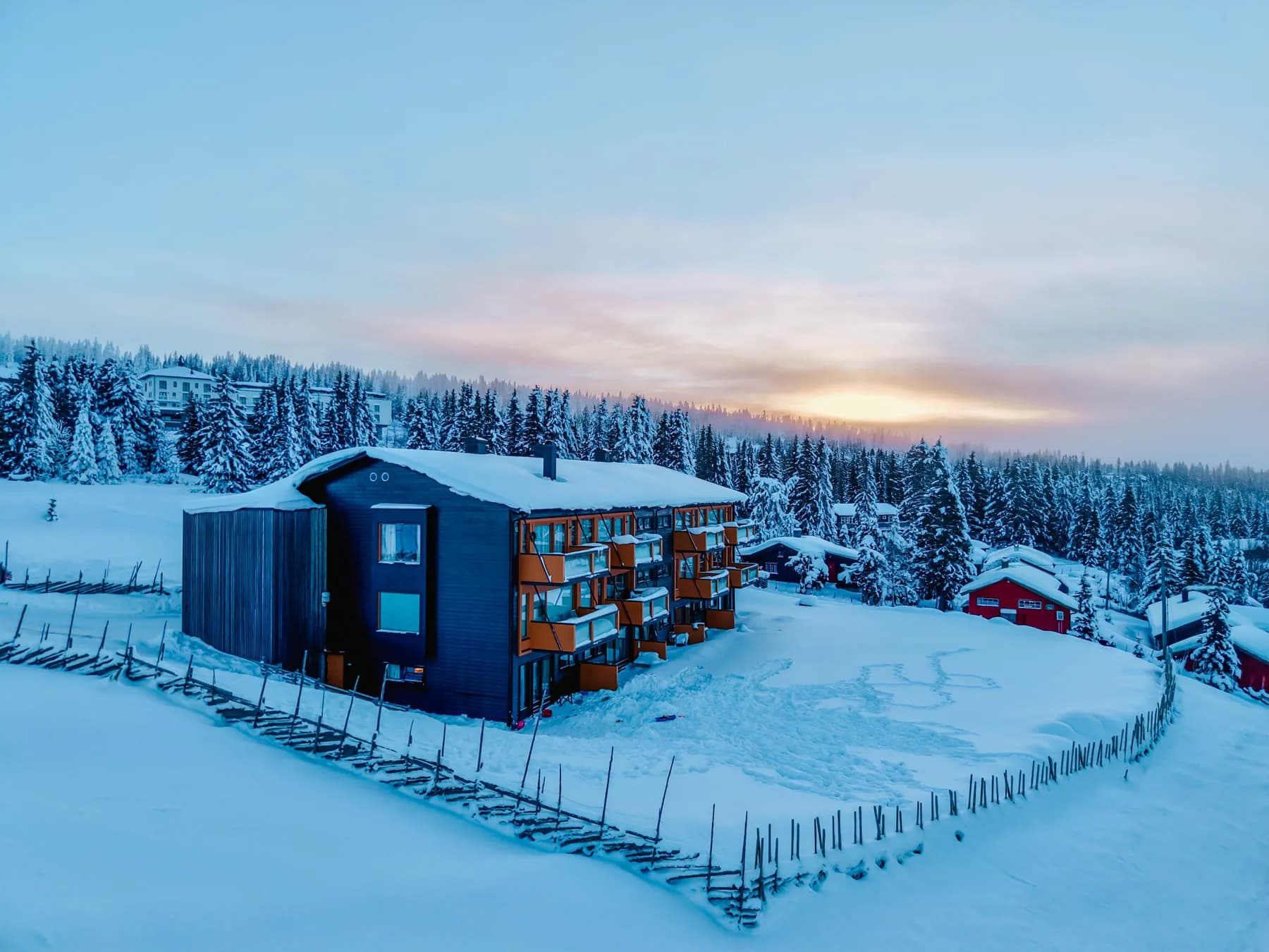 Dronebilde av leilighetsbygget på Nordseter i blå time, med snødekt skog og soloppgang bak