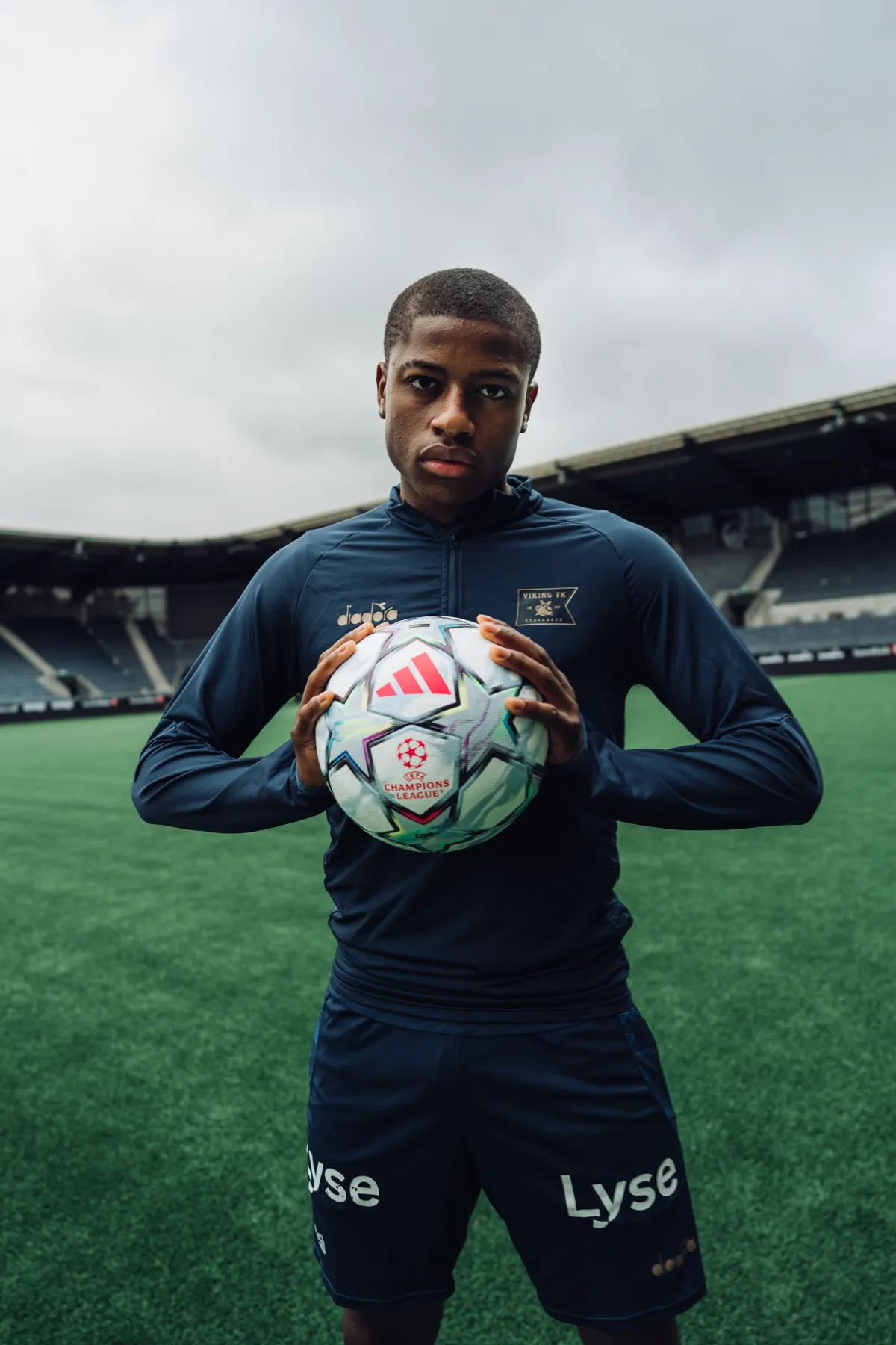 Stående portrett av Tobias Moi med ballen, med stadion og skyer bak