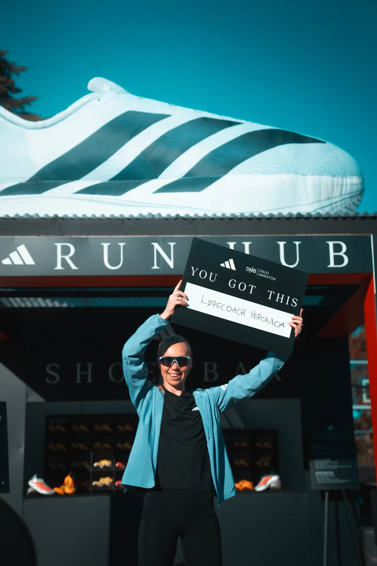 Veronica Undseth holder et cheering sign under den oppblåste Adizero Evo SL på taket av Run Hub