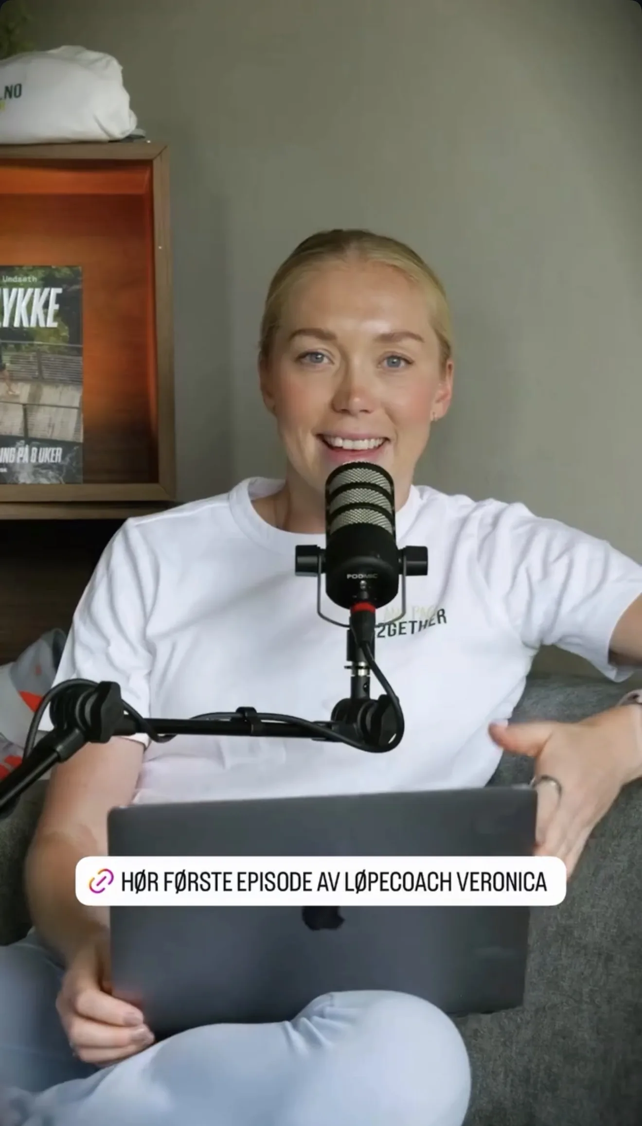 Veronica Undseth sitter i sofaen med en podcastmikrofon på stativ foran seg og en laptop i fanget.